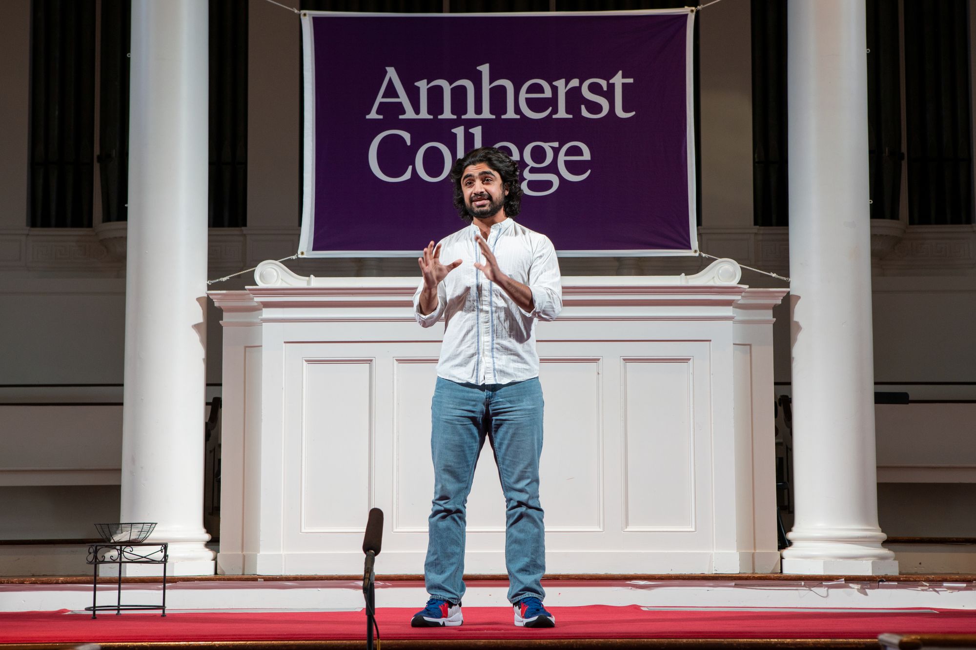 The image depicts Daniyal Ahmad Khan speaking and using hand gestures onstage at Johnson Chapel.