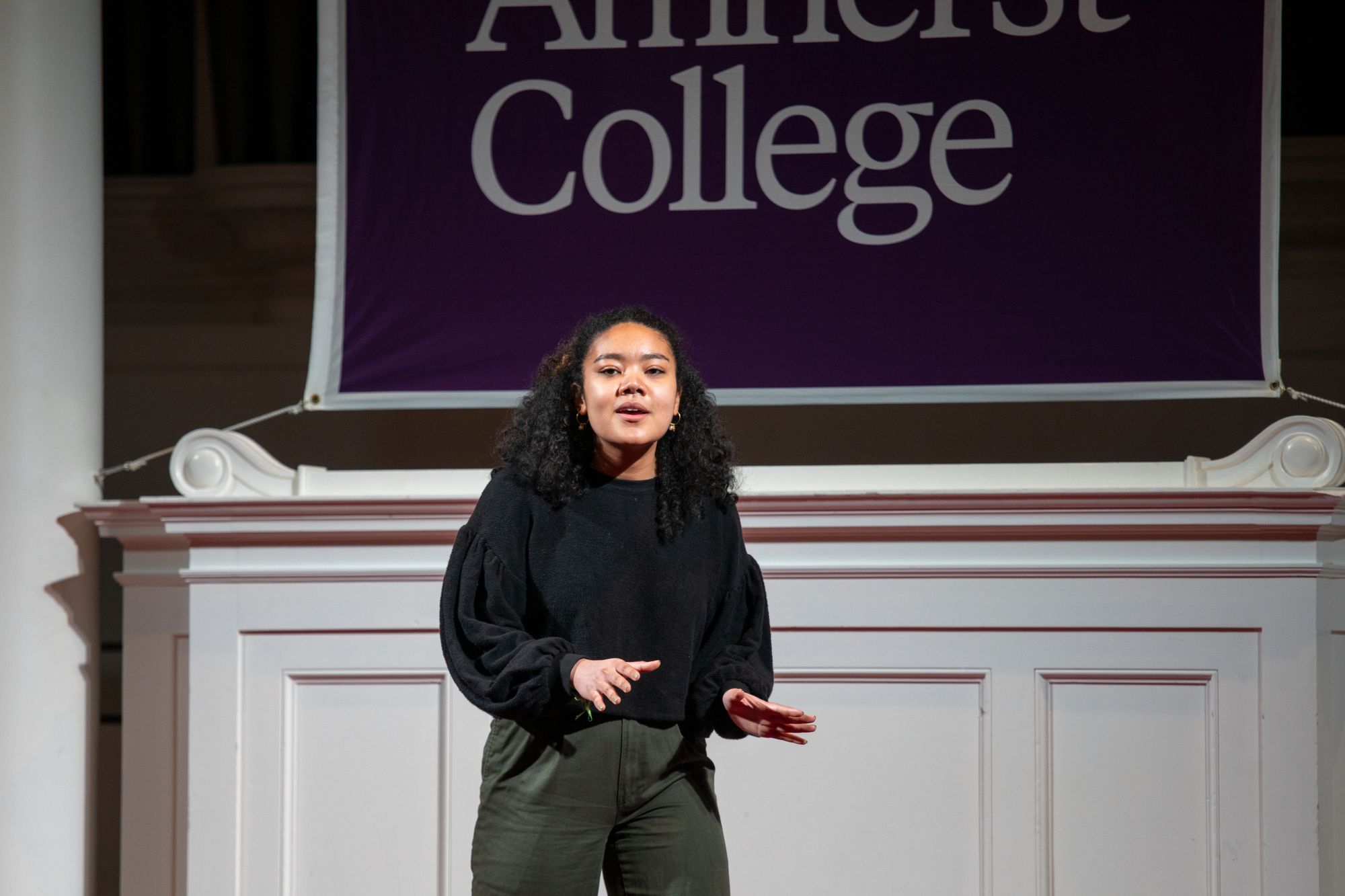 The image depicts Mia Griffin speaking and using hand gestures on the stage at Johnson Chapel.