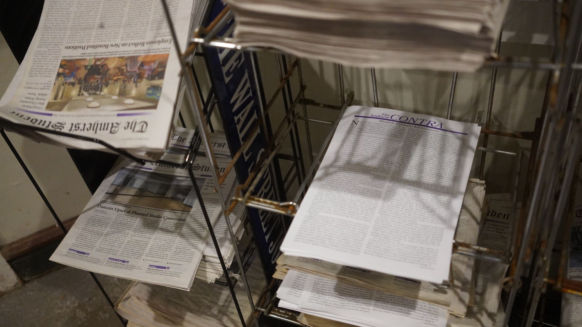 The image depicts a stack of several copies of The Contra sitting on a newspaper rack in Valentine Dining Hall