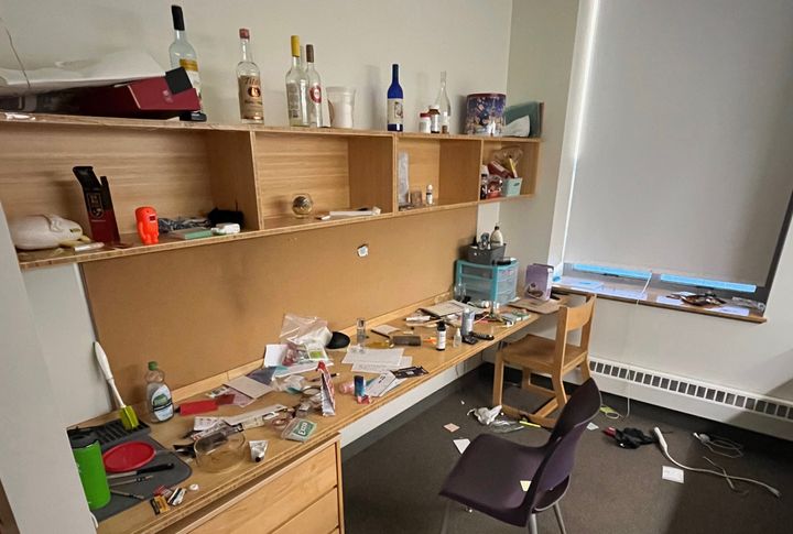 The image depicts an Amherst dorm room littered with bottles, trash, and discarded personal belonging