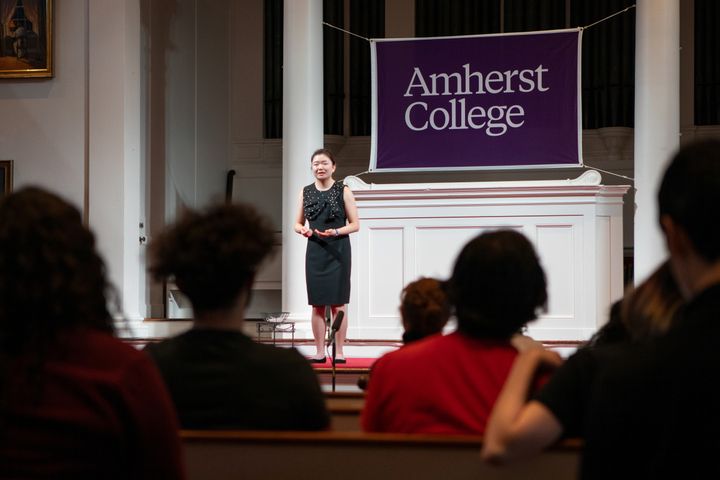 The image depicts Karen Lee in front of an intent audience, speaking on the stage at Johnson Chapel.